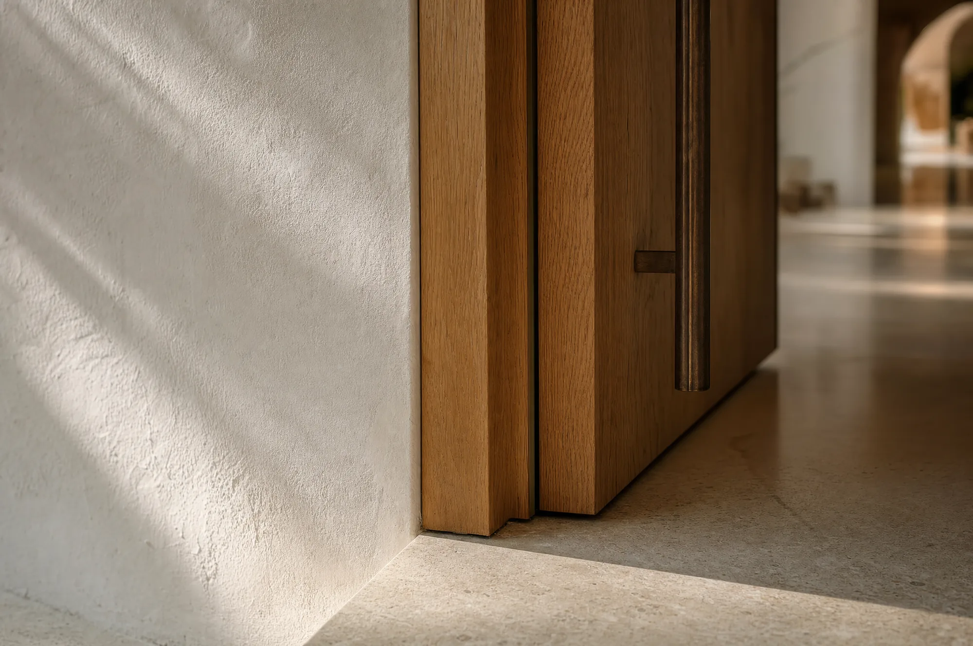 Close detail of a villa threshold: hand-troweled lime plaster meeting a solid oak door reveal and a honed limestone floor