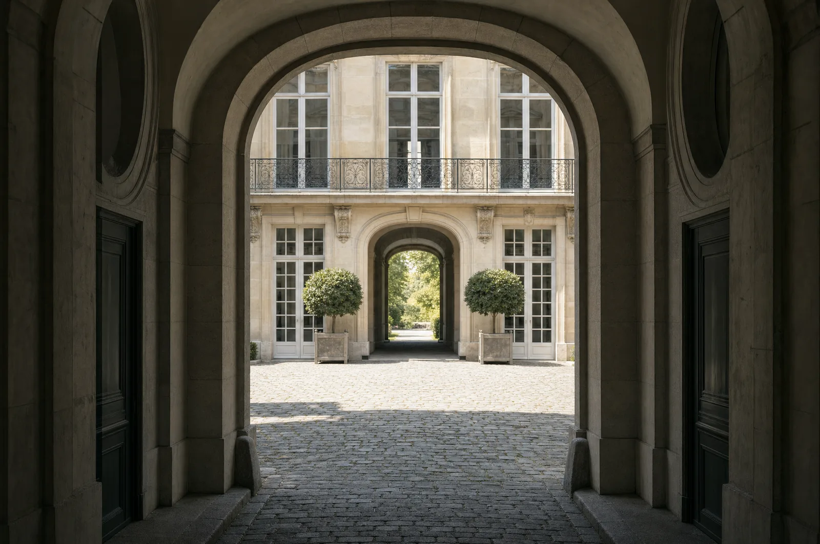 Cour pavee d'un hotel particulier parisien vue depuis le porche voute, avec une seconde arche ouvrant sur le jardin